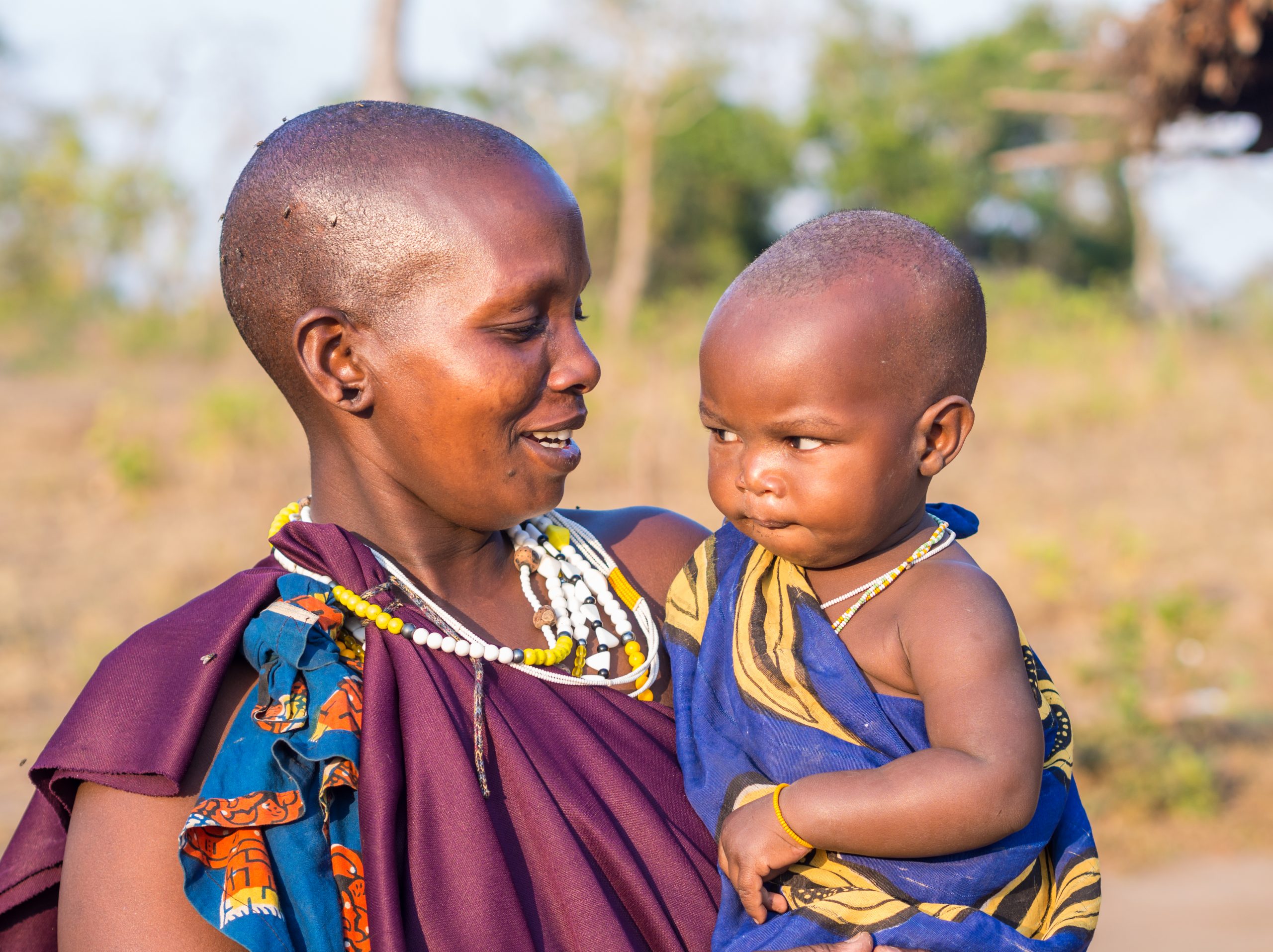 Handeni, Tanzania - August 01, 2015: Maasai mother with her child standing in front of a traditional house in their boma (village) in Tanzania, Africa, on a normal evening.