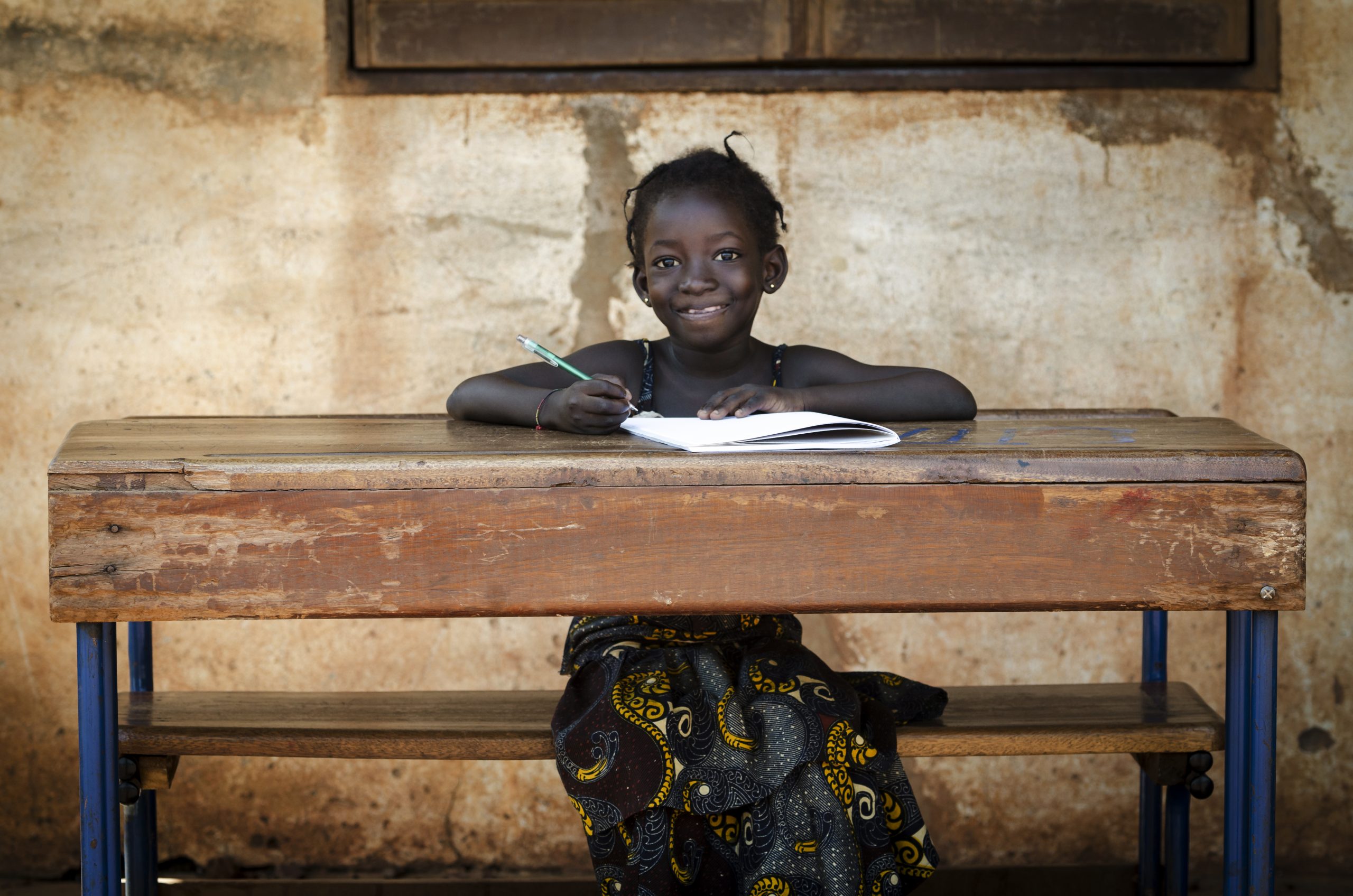 Little super cute African girl sitting in her desk, proudly writing a letter at school in Bamako, Mali.