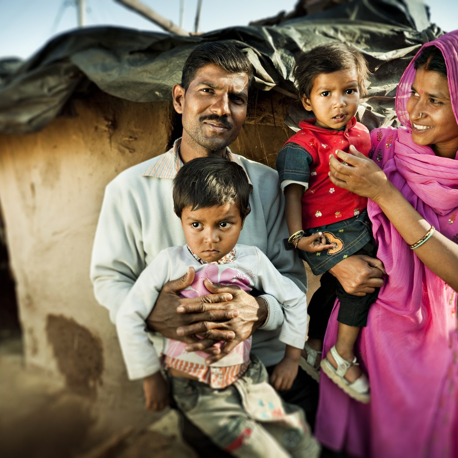 Real people from rural India: Happy parents with their children near their adobe house in slum colony of village.